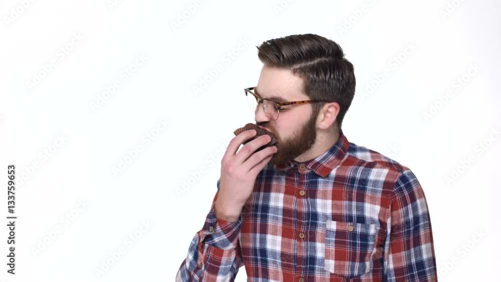 Terrified young bearded man in eyeglasses holding fist near face and staring at you while standing against white background Terrified young bearded man in eyeglasses holding fist near face and staring at you while standing against white background