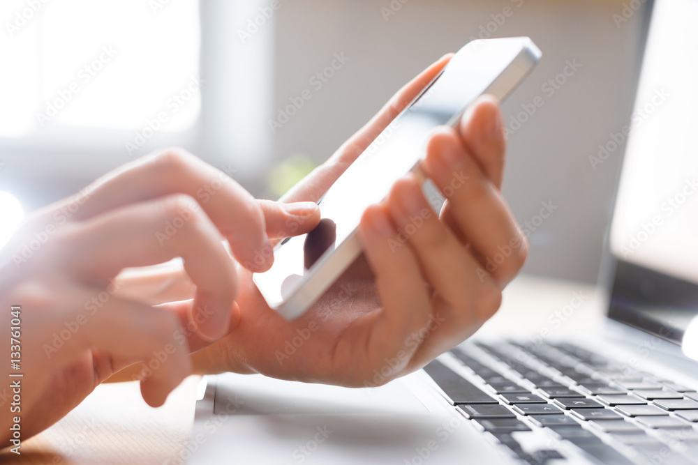 Hands using phone for searching, online shopping, business in front of laptop in simple interior Hands using phone for searching, online shopping, business in front of laptop in simple interior