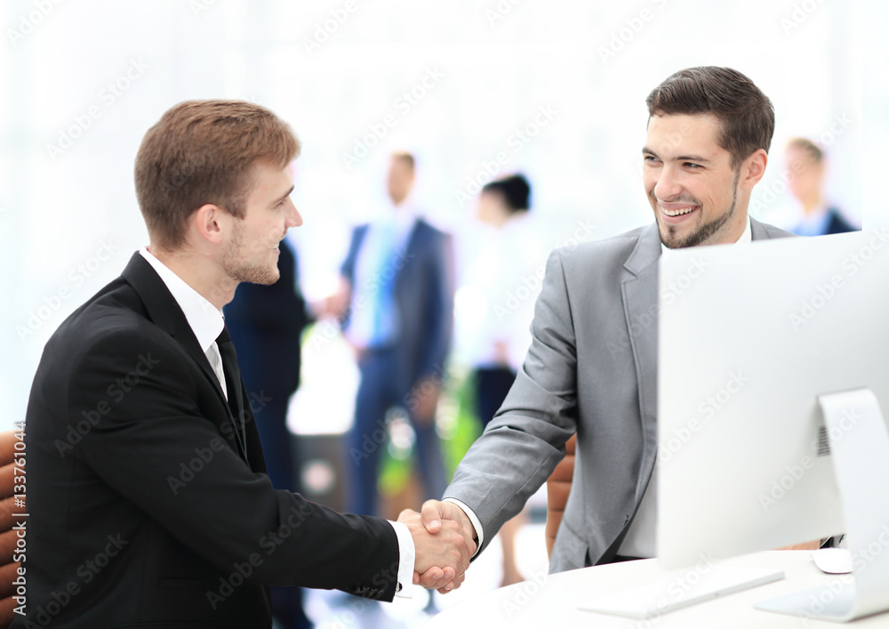 Two happy young men shaking hands while sitting at the office Two happy young men shaking hands while sitting at the office