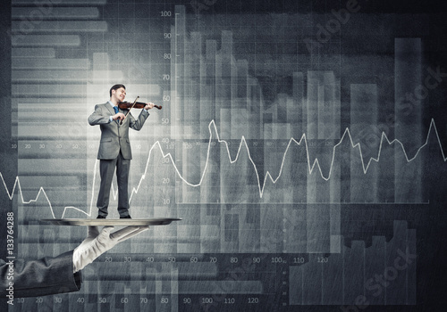 Businessman on metal tray playing violin against graphs and diagrams background