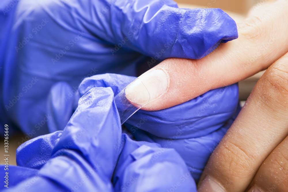 Manicure specialist care by finger nail in beauty salon.Gel nails. Finger closeup isolated on blue gloves background. Manicurist uses professional manicure tool. Manicure specialist care by finger nail in beauty salon.Gel nails. Finger closeup isolated on blue gloves background. Manicurist uses professional manicure tool.