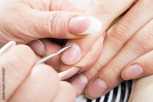 Manicure specialist care by finger nail in beauty salon. Manicurist uses professional manicure tool.
