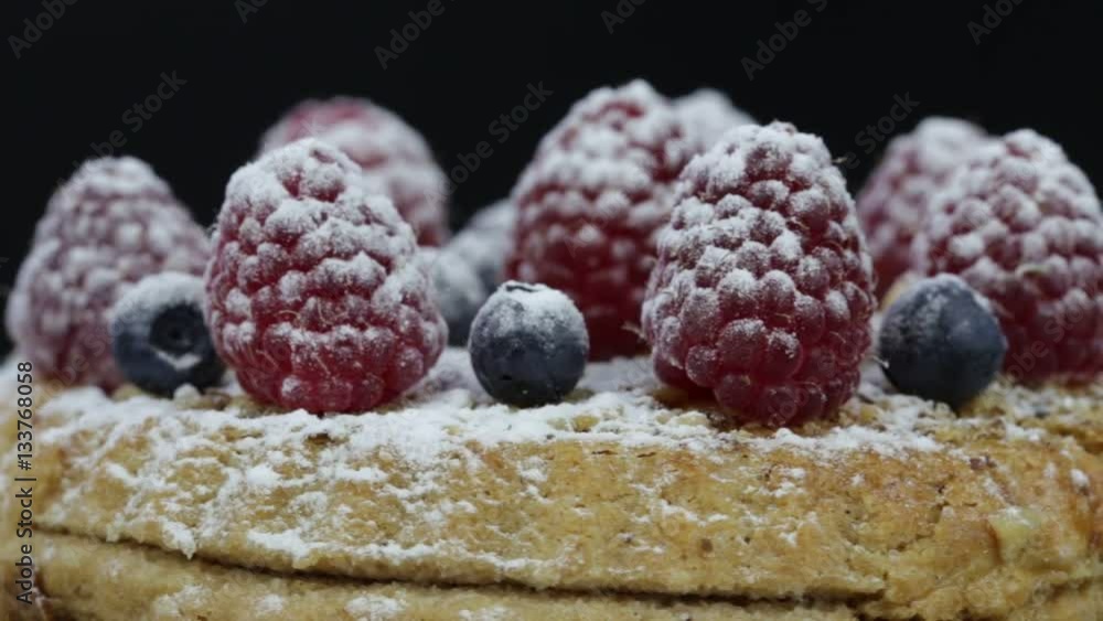 Cake with raspberries, blueberries, sea buckthorn sprinkled with powdered sugar on a black plate rotates Cake with raspberries, blueberries, sea buckthorn sprinkled with powdered sugar on a black plate rotates