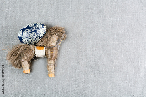 straw horse with a painted egg on a gray background