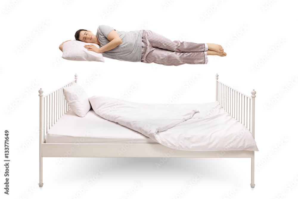 Young man sleeping and floating above a bed