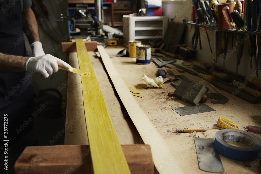 A man examining a piece of wood at a workbench. A man examining a piece of wood at a workbench.