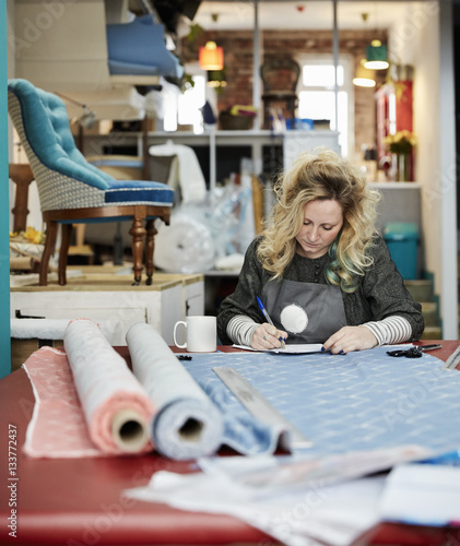 A woman preparing, measuring and cutting upholstery fabric on a workbench.  photo