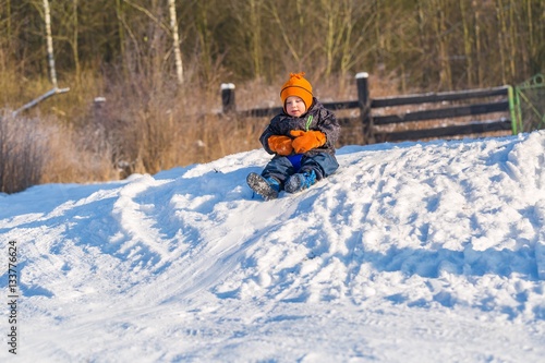 Happy little caucasian boy downhill on plastic slider or sledge