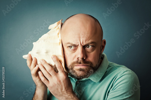Bearded middle-aged  man with shell listening noise of sea