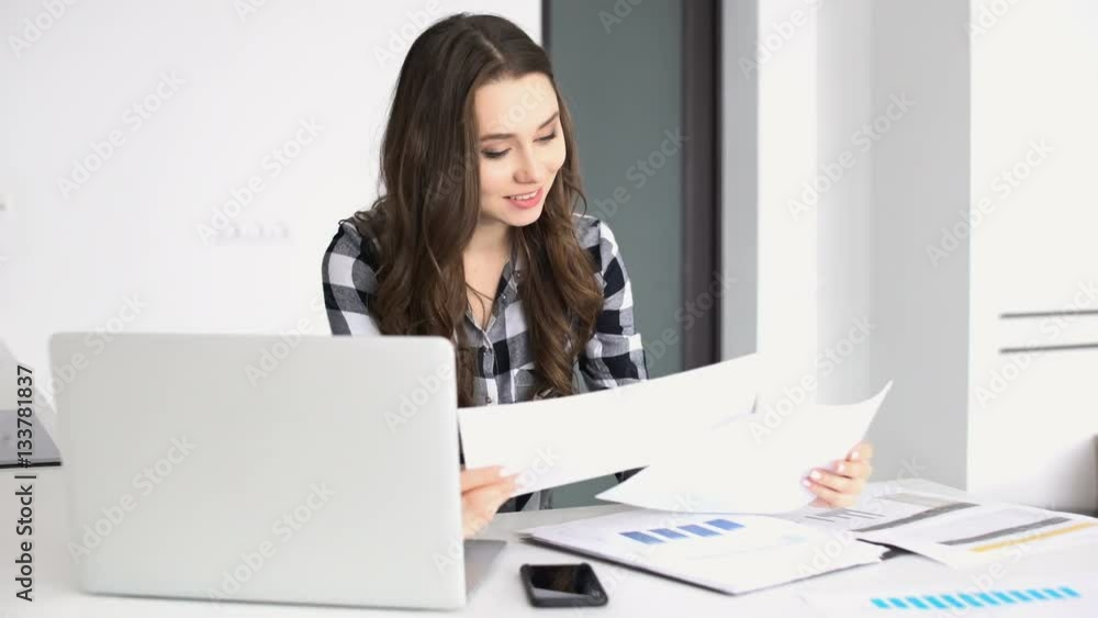 Smiling casual woman working with blueprints and laptop at home Smiling casual woman working with blueprints and laptop at home