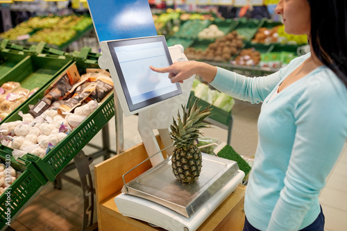 Fototapeta woman weighing pineapple on scale at grocery store