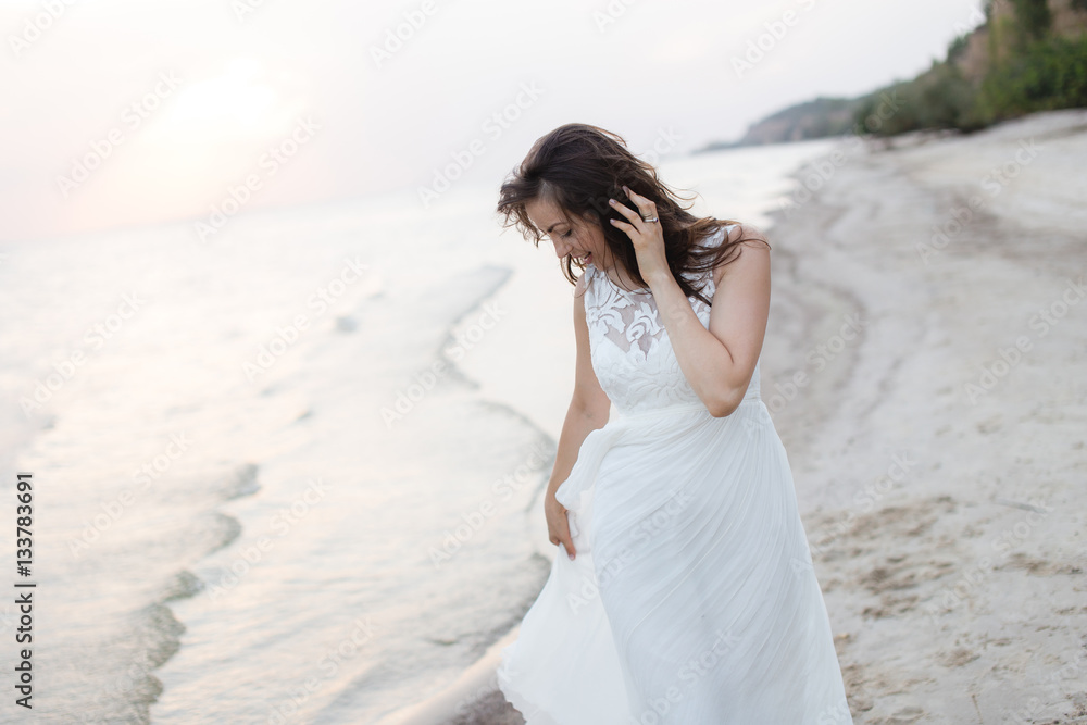 Beautiful young brunette woman in white long dress at the sea shore