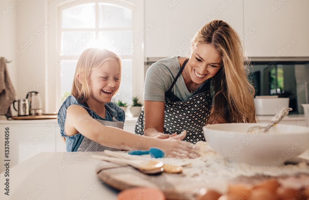 Happy young girl with her mother making dough - obrazy, fototapety, plakaty 
