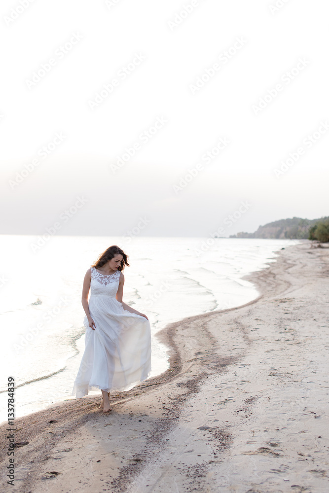 Beautiful young brunette woman in white long dress at the sea shore Beautiful young brunette woman in white long dress at the sea shore
