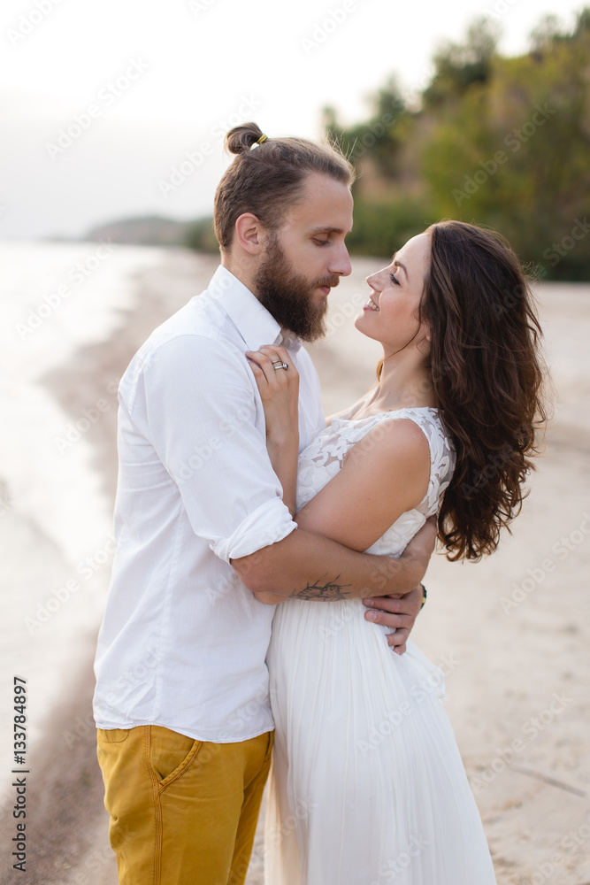 Beach honeymoon couple kissing and hugging on white sand beach. Newlyweds happy in love relaxing on summer holidays. Travel vacation concept. Beach honeymoon couple kissing and hugging on white sand beach. Newlyweds happy in love relaxing on summer holidays. Travel vacation concept.