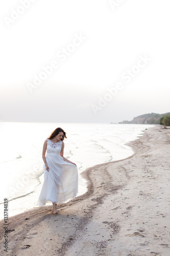 Beautiful young brunette woman in white long dress at the sea shore © muzhchil
