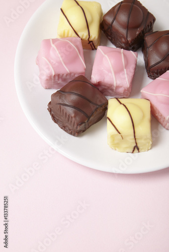 A plate full of fondant fancies cakes on a pastel pink background with empty space below
