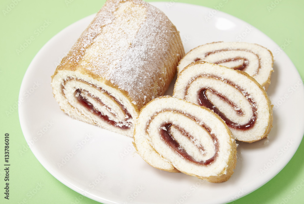 A strawberry jam Swiss roll cake on a pastel green background