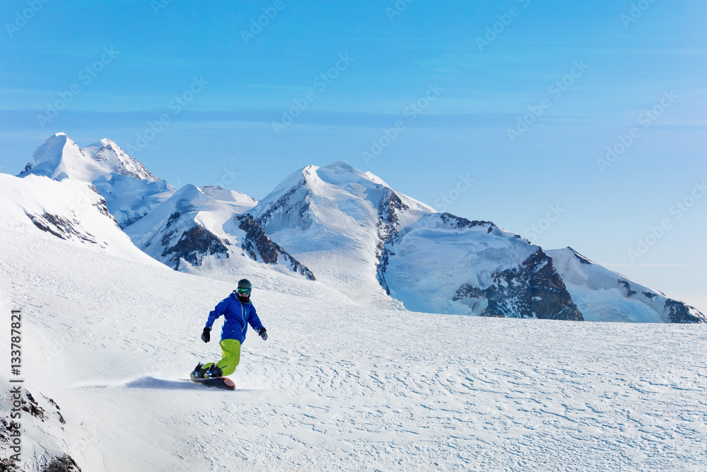 Male snowboarder on the slope with mountain peaks on background