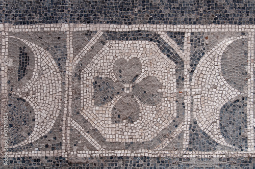 Antico pavimento in mosaico con le tessere in bianco e nero che compongono il disegno con i fiori e mezzalune photo