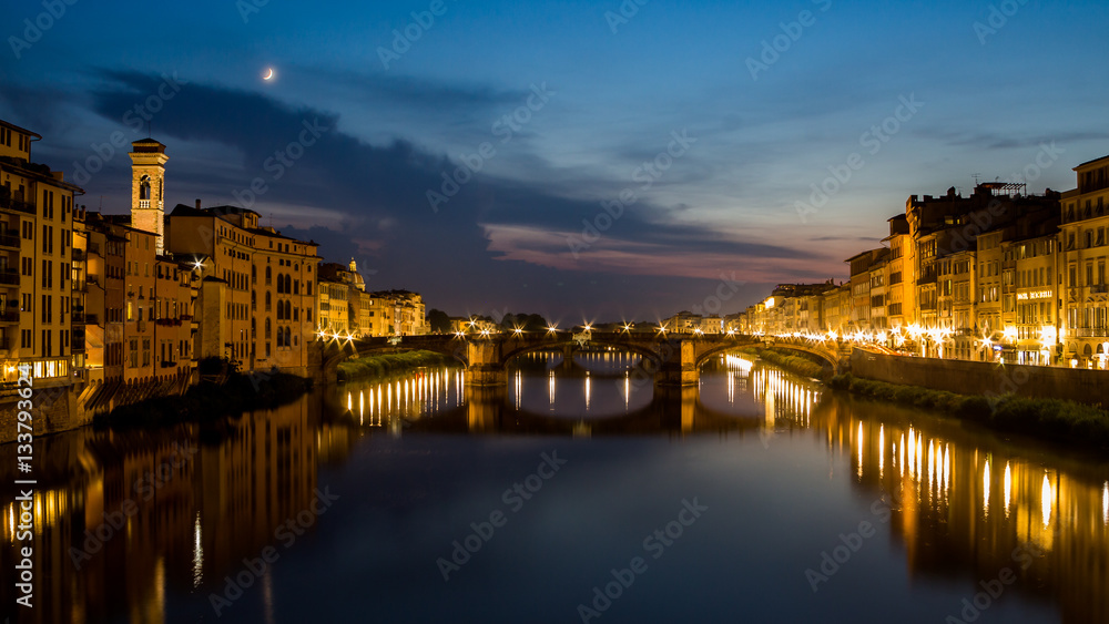 Night scene with a beautiful skyline with a moon. Lights reflect on a soft tranquil waters of a river. Residential view on both sides of the river embankments. 