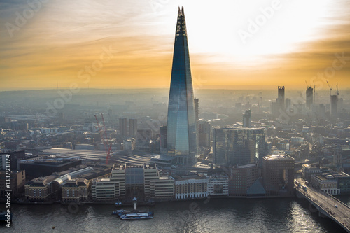 One of the tallest buildings in London - The Shard tower rising above the river Thames and everything around. Foggy skyline is painted with beautiful orange sunset. photo