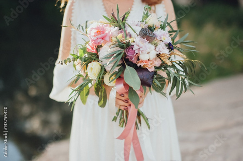 The bride with a bouquet on beautiful large lake background at sunset. Rustic Wedding