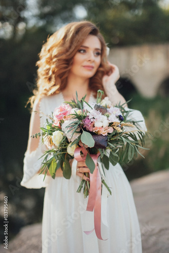 The bride with a bouquet on beautiful large lake background at sunset. Rustic Wedding