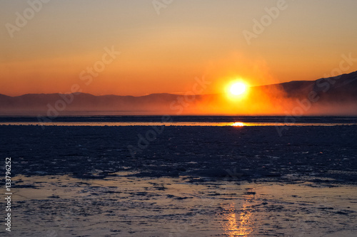 Sun just over surface of freezing lake in mist from vaporization  just before sunset 