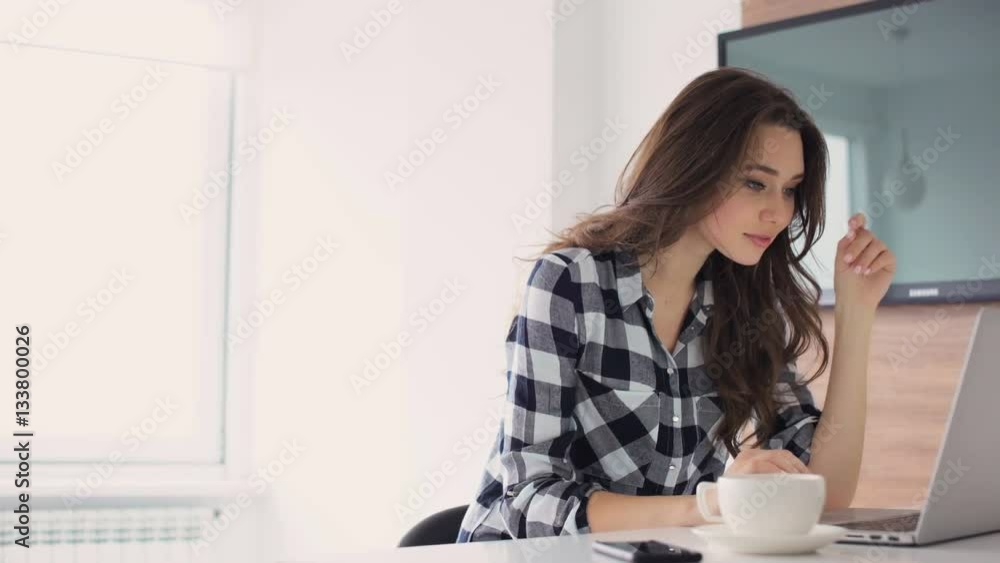Smiling happy woman talking on mobile phone while using laptop at home 