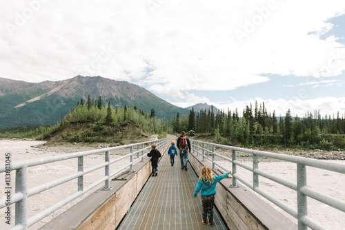Family crossing footbridge towards woodland landscape 