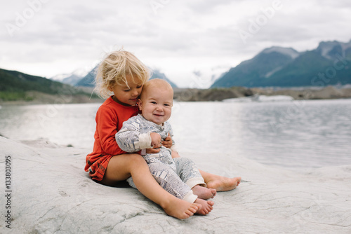Girl with baby boy sitting at lakeside