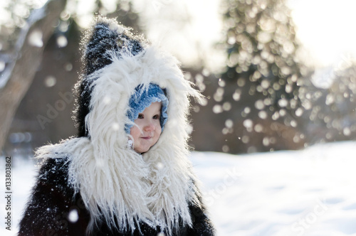 Little girl in fox fur coat looking at the falling snow in winte