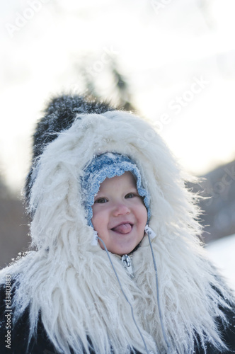 Little girl in a fur coat walks in the winter park