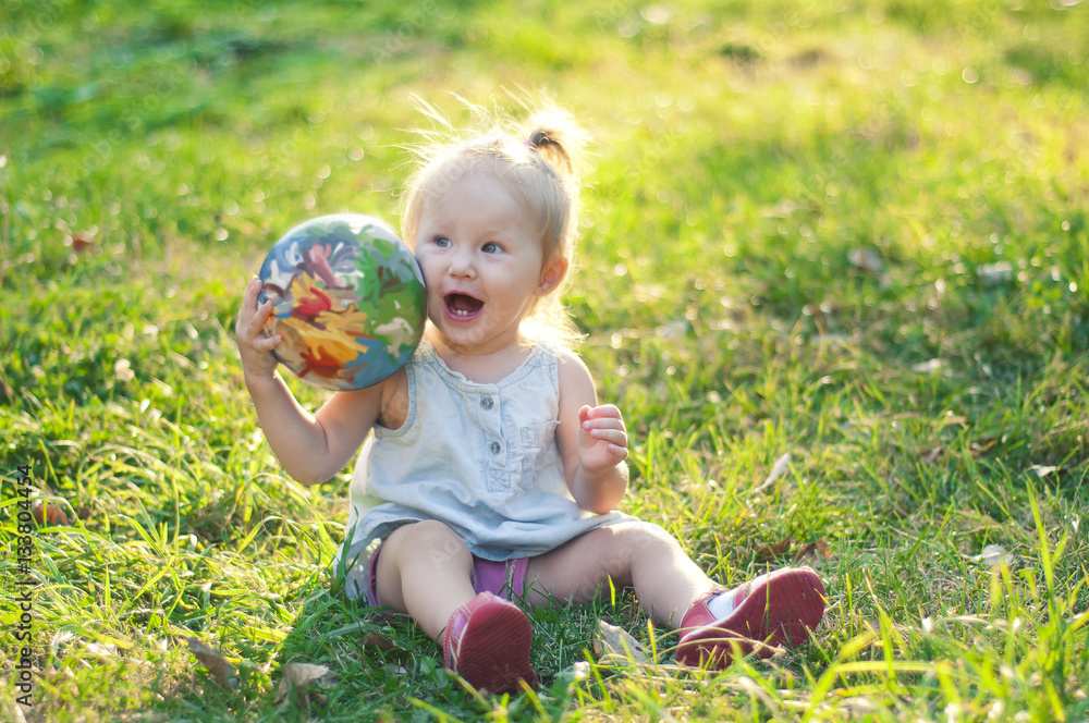 Cheerful little girl playing with a ball in a summer park on the Cheerful little girl playing with a ball in a summer park on the