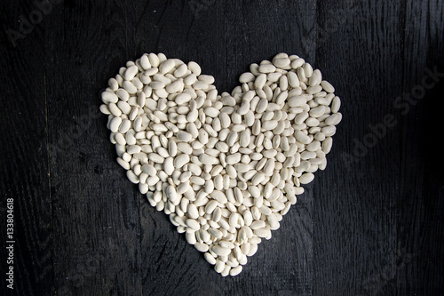 Valentine's day heart made from white bean on dark wooden background