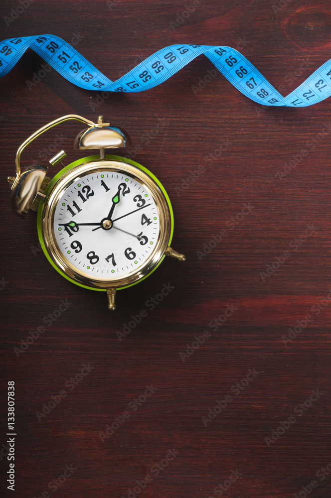measuring tape and alarm clock on the wooden background