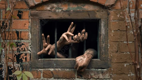 Two pairs of hands clawing the air from dark barred window photo