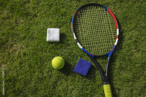 Tennis ball, racket and wristbands on grass field ground under sunlight
