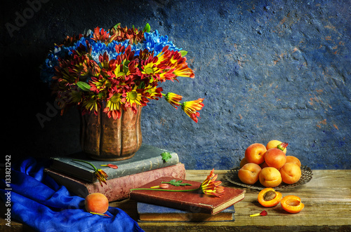 Classic still life with Daisy and Blanket flowers placed together in copper vase on old books,scarf, apricots on rustic wooden background..