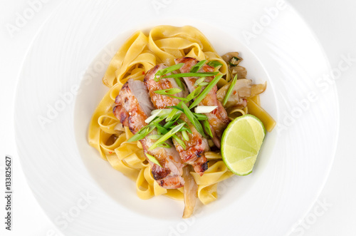 Pasta Fettuccine and caramelized pork with green onions and lime on a plate on a white background, top view