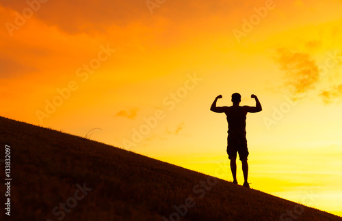 Fit strong man flexing against a beautiful sunset. © kieferpix