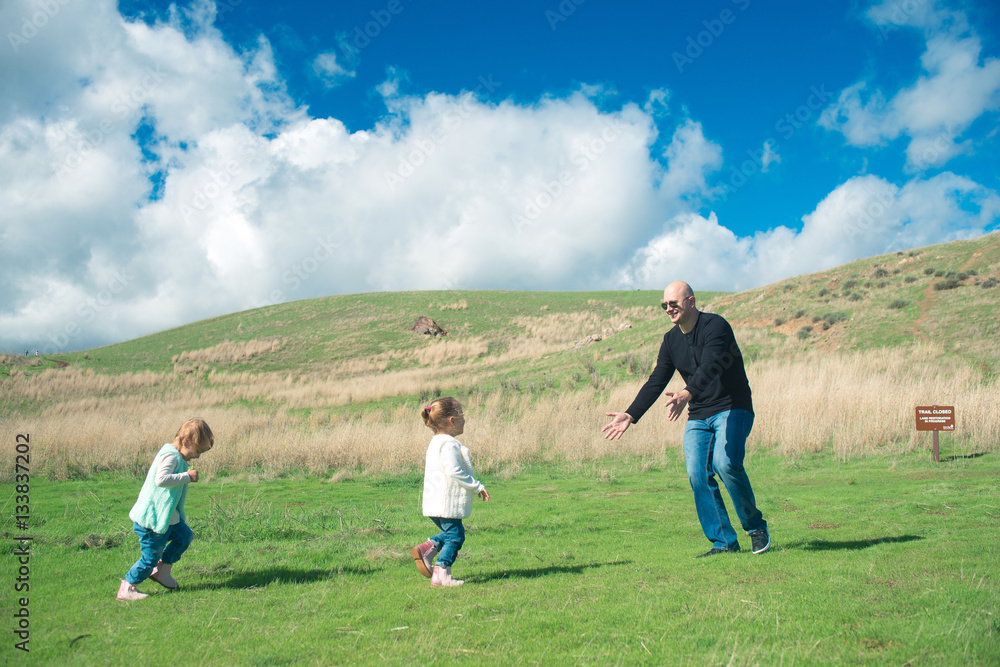 Smiling father playing with his two laughing daughters in the pa