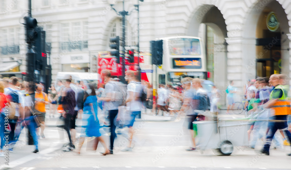 Fototapeta premium Piccadilly circus with lots of people, tourists and Londoners crossing the junction. Red bus at the background. Blurred type image 