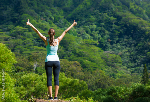 Happy active fit woman standing on a mountain with arms up in the air. 