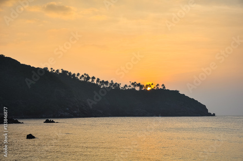 Sunset on a tropical island, palm trees silhouettes on the rocks