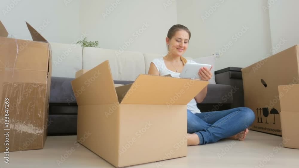 Dolly shot of young woman using digital tablet while packing things and moving to a new apartment Dolly shot of young woman using digital tablet while packing things and moving to a new apartment