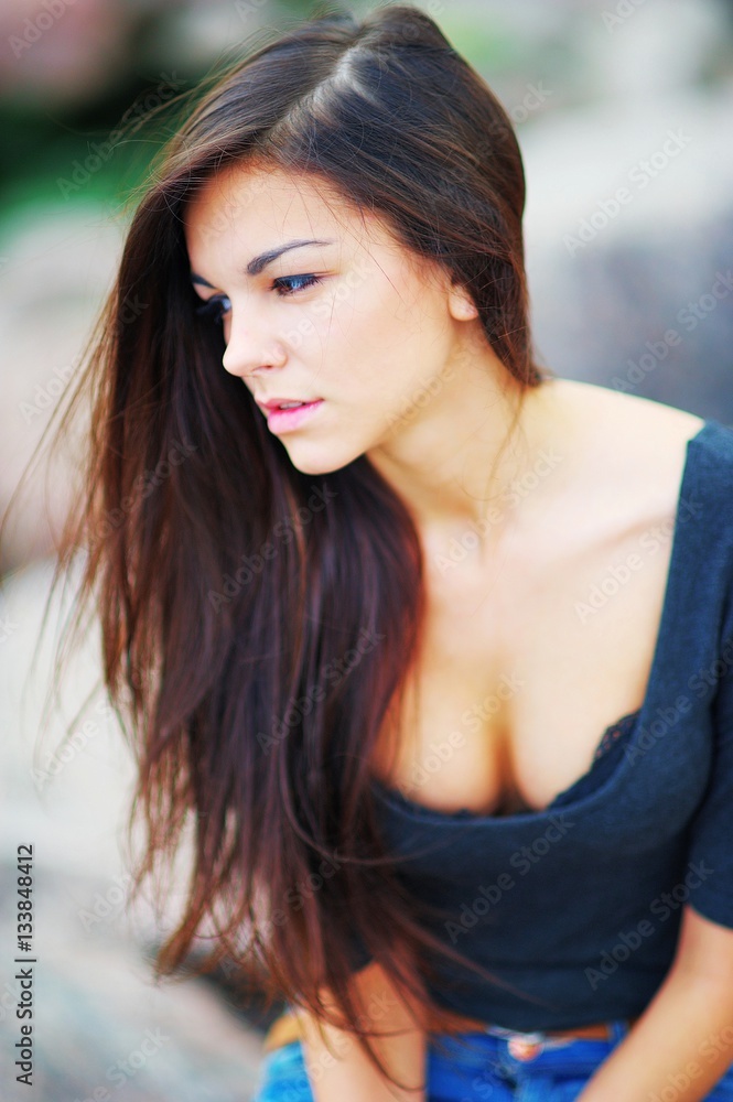 Portrait of young beautiful long-haired brunette woman in a black shirt with a deep neckline on blurred background, close up