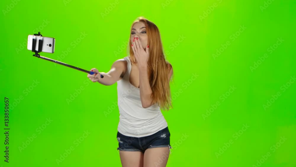 Redheaded girl makes various photos using selfie stick. Green screen Redheaded girl makes various photos using selfie stick. Green screen