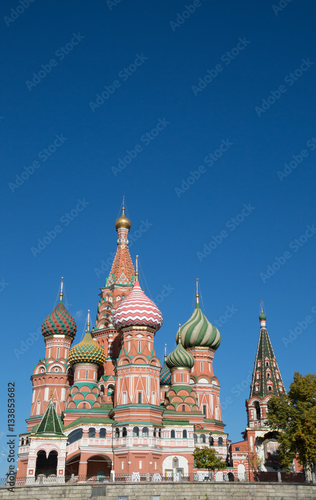 St. Basil's Cathedral on Red Square showing decorative red brick facade and colorful onion domes topped with Orthodox crosses against a deep blue sky. 